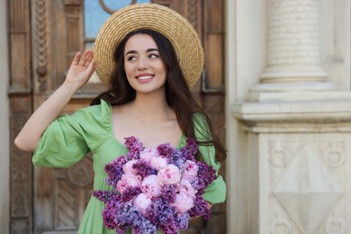 Beautiful woman with bouquet of spring flowers near building outdoors, space for text