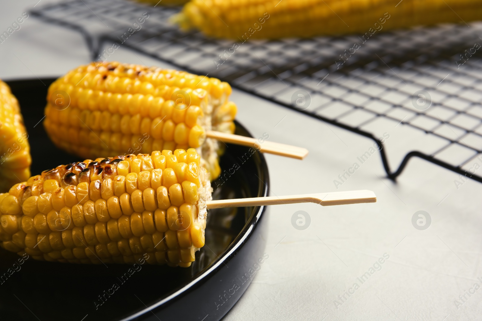 Photo of Ceramic plate with grilled corn cobs on light background, closeup