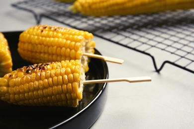 Ceramic plate with grilled corn cobs on light background, closeup