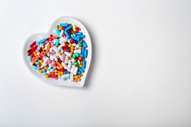 Photo of Heart shaped plate with different pills on white background. Cardiology service