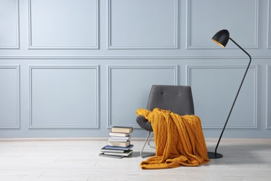 Photo of Comfortable armchair with blanket, books and lamp near grey wall indoors, space for text