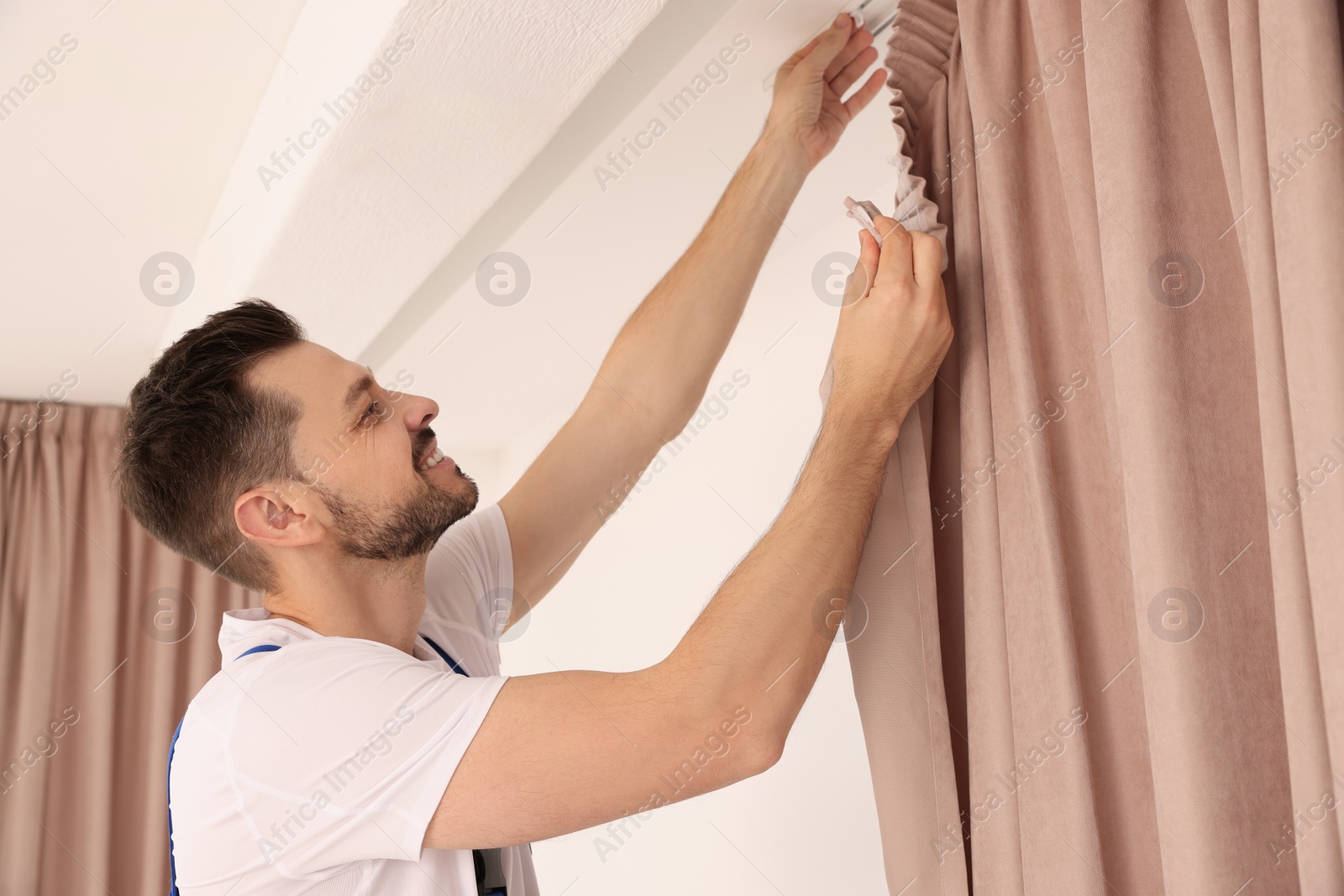 Photo of Worker in uniform hanging window curtain indoors