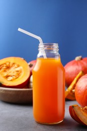 Photo of Tasty pumpkin juice in glass bottle and pumpkins on light grey table against blue background
