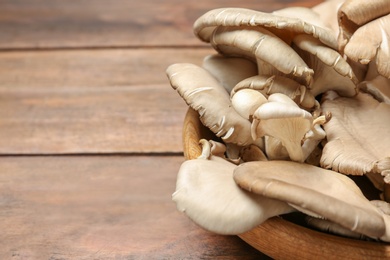 Bowl with delicious organic oyster mushrooms on wooden background, closeup. Space for text