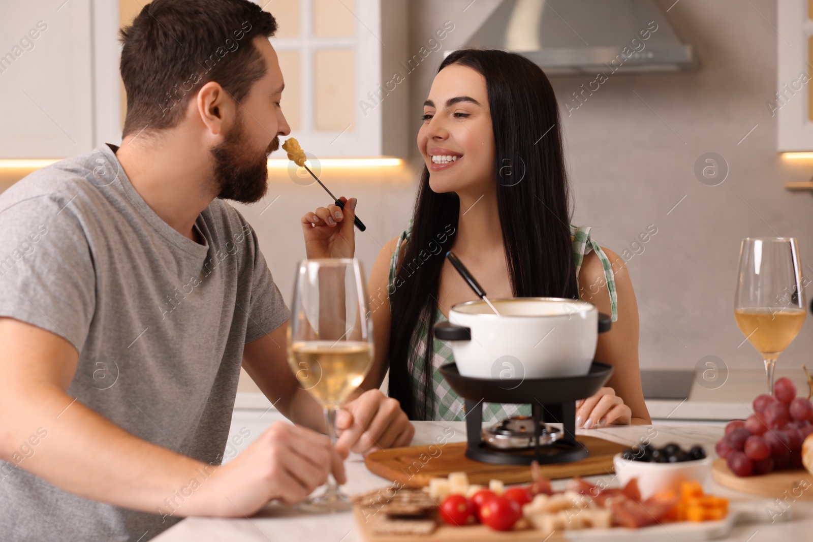 Photo of Affectionate couple enjoying cheese fondue during romantic date in kitchen