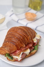 Tasty croissant with brie cheese, ham and bacon on white table, closeup
