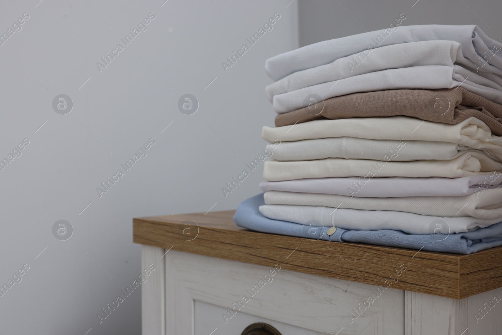 Photo of Different folded shirts on chest of drawers near grey wall, space for text. Organizing clothes