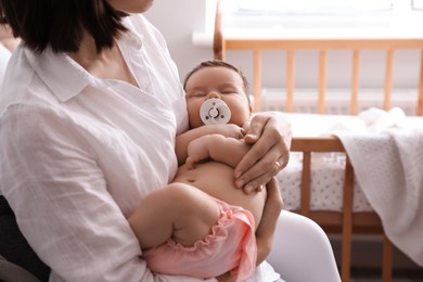 Mother holding her cute little baby with pacifier at home, closeup