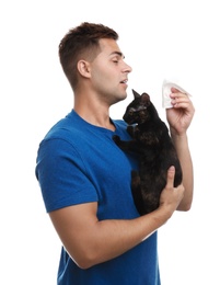 Young man with cat suffering from allergy on white background