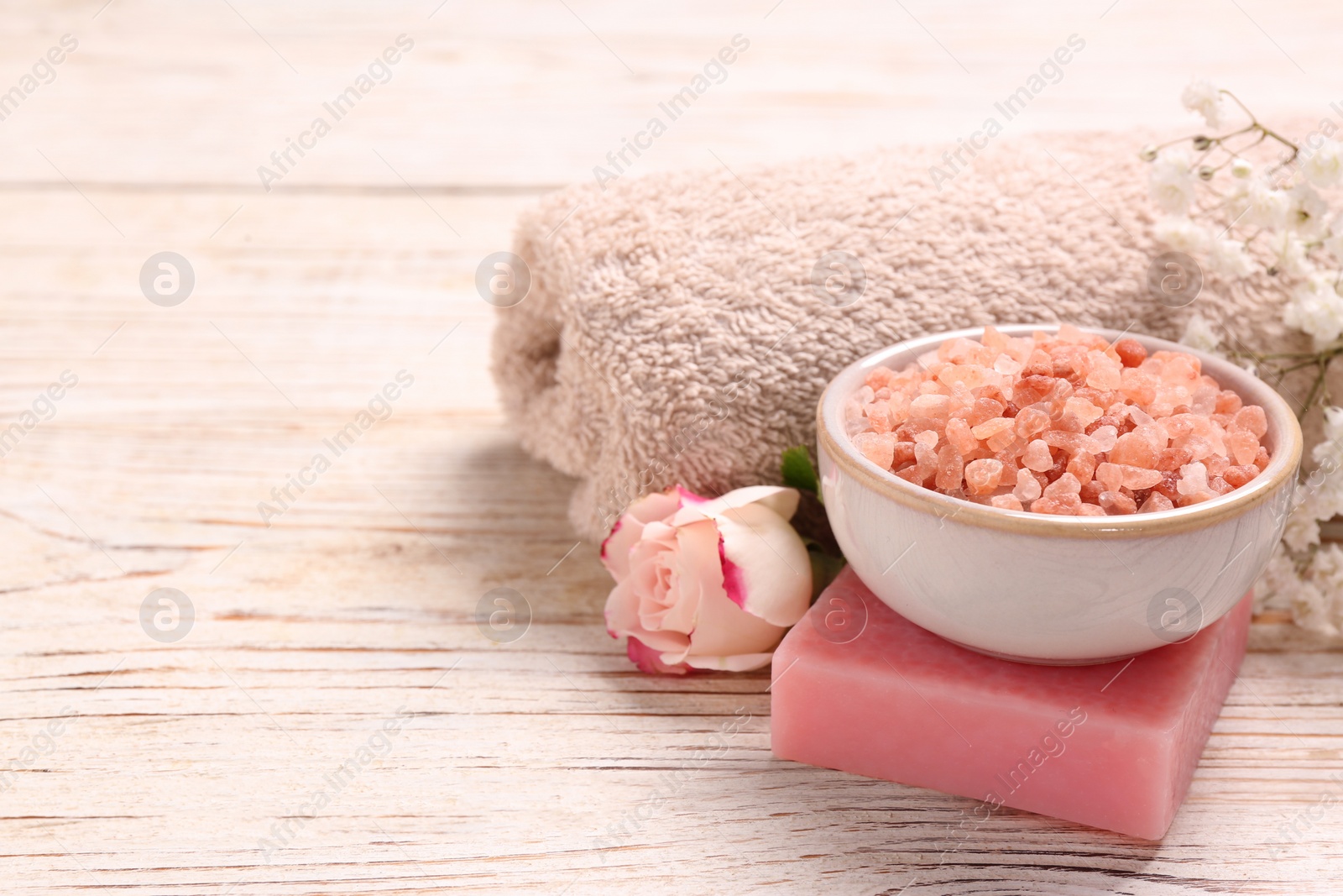 Photo of Bowl with sea salt, soap bar and towel on white wooden table. Space for text