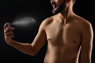 Photo of Man spraying luxury perfume on dark background, closeup