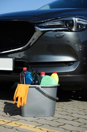 Car cleaning products in bucket near automobile outdoors on sunny day