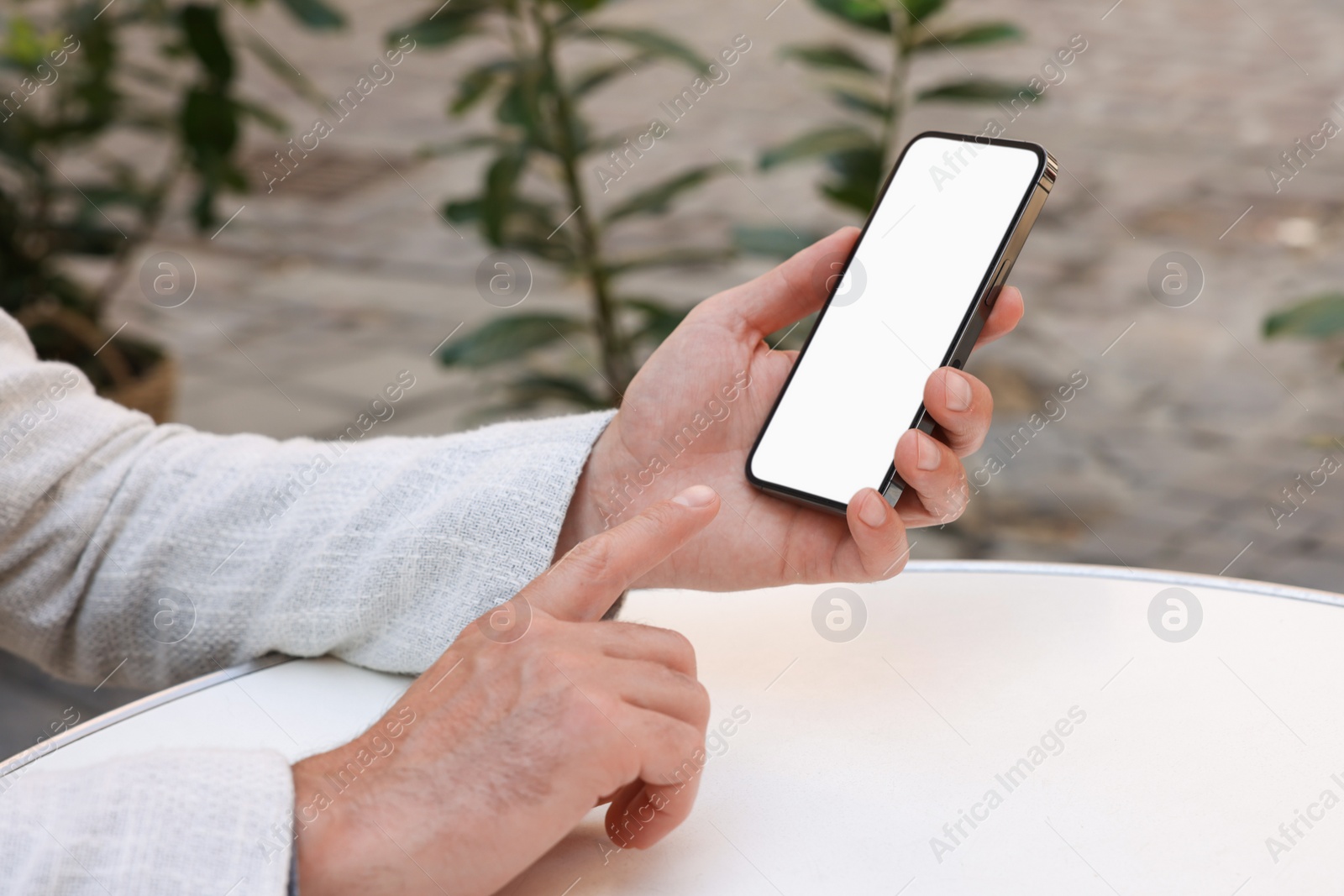 Photo of Man using smartphone at white table outdoors, closeup