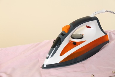 Photo of Board with modern iron and shirt on beige background. Laundry day