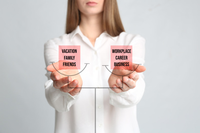 Work-life balance concept. Woman demonstrating illustration of scales with words on light background, closeup