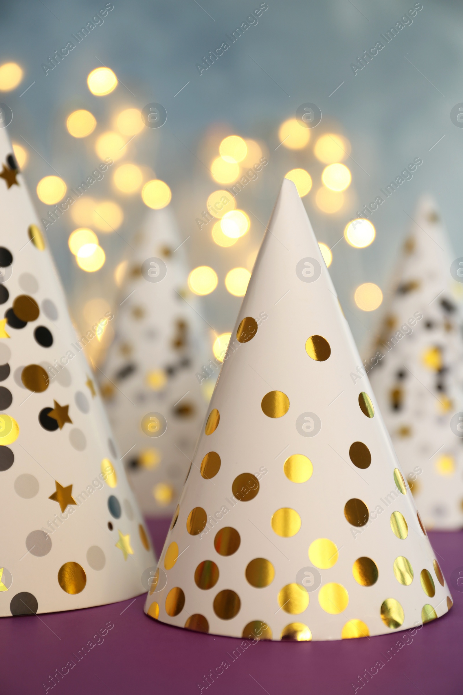 Photo of Beautiful party hats on purple table against blurred lights