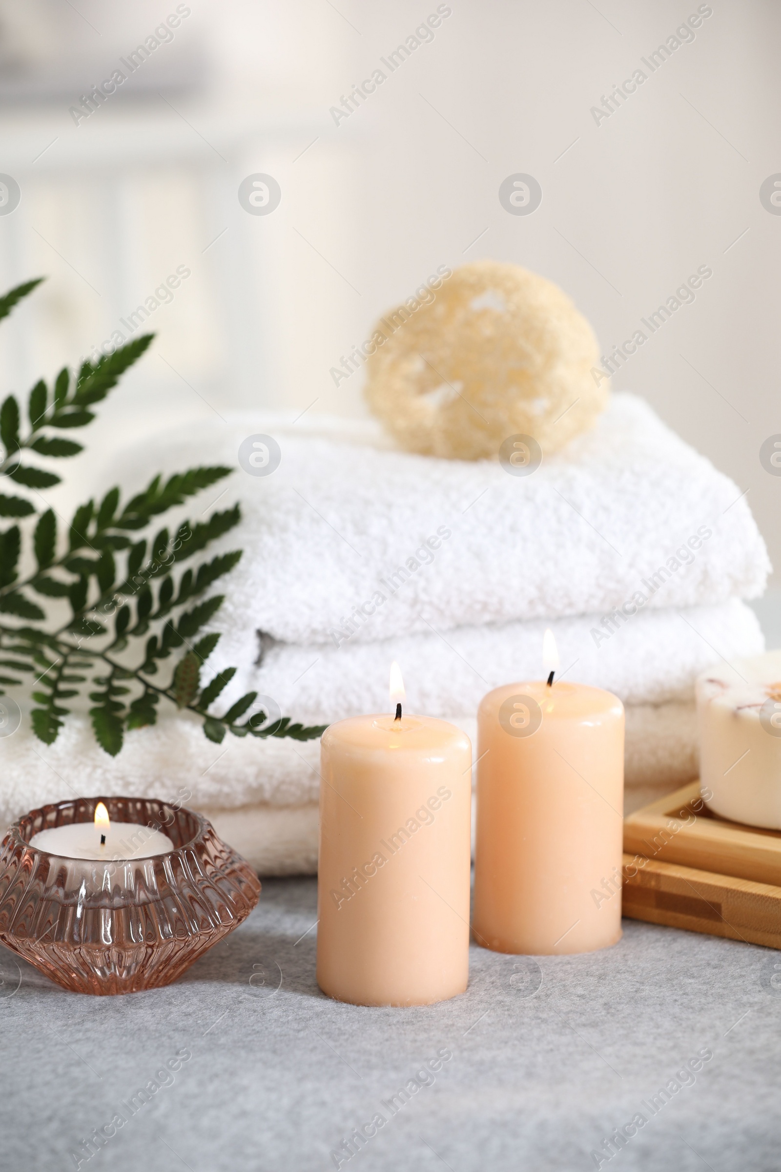 Photo of Spa composition. Burning candles, soap, towels and loofah on soft grey surface