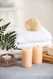 Photo of Spa composition. Burning candles, soap, towels and loofah on soft grey surface