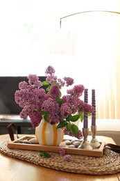 Beautiful lilac flowers in vase and candles on table at home