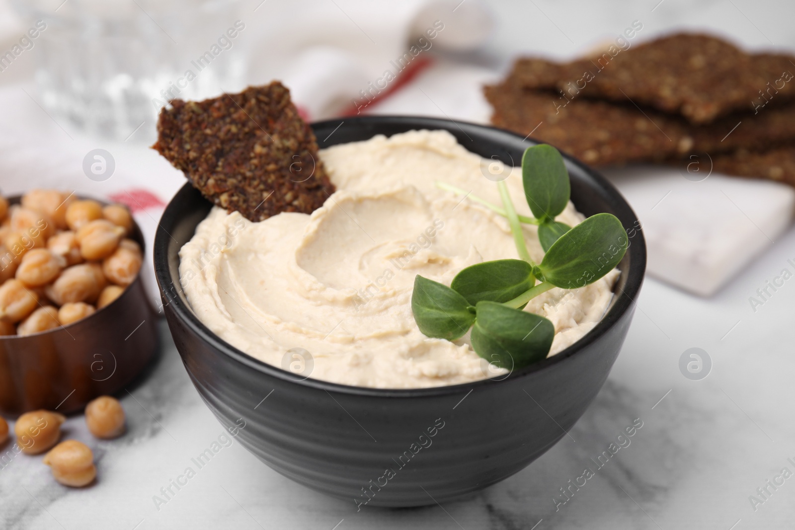 Photo of Delicious hummus with crispbread served on white marble table, closeup