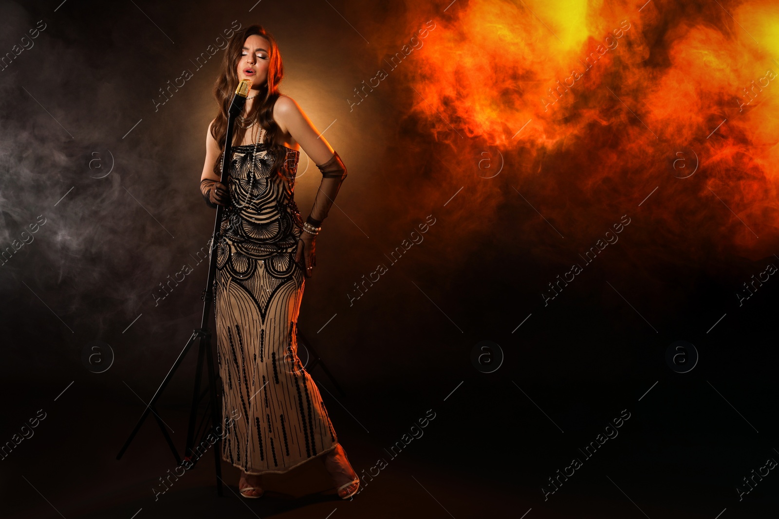 Photo of Beautiful young woman with microphone singing in color lights and smoke, space for text