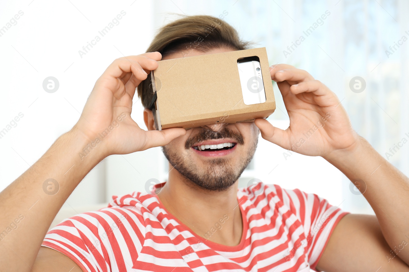 Photo of Young man using cardboard virtual reality headset at home