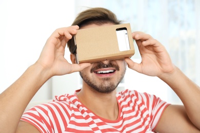 Photo of Young man using cardboard virtual reality headset at home