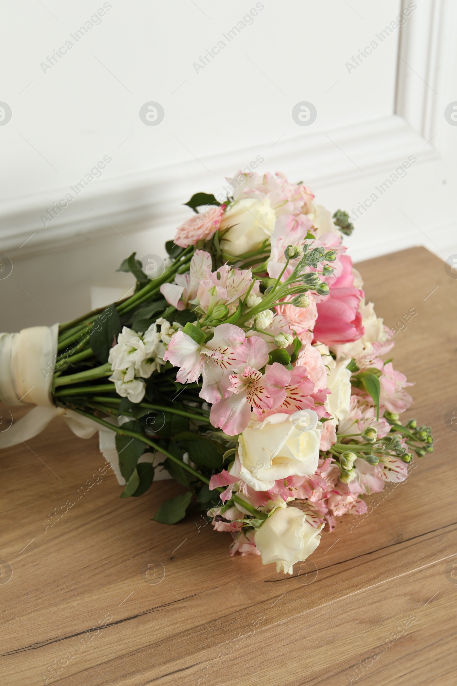 Photo of Beautiful bouquet of fresh flowers on wooden table near white wall