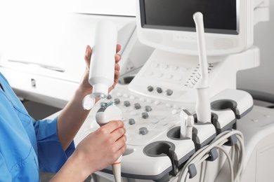 Sonographer covering ultrasound machine probe with gel in clinic, closeup