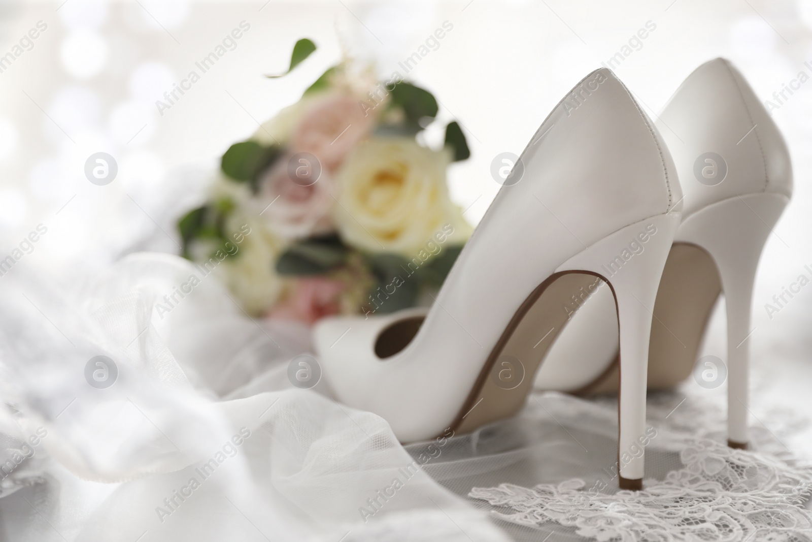 Photo of Pair of white high heel shoes, veil and wedding bouquet on light background