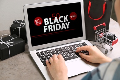 Photo of Woman using laptop with Black Friday announcement at grey table, closeup