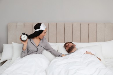 Emotional woman waking up man in bedroom. Being late concept
