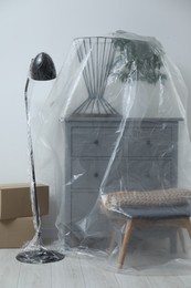 Photo of Modern furniture, houseplant covered with plastic film and boxes at home