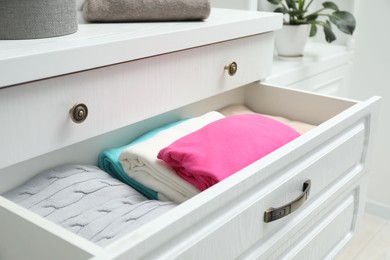 Photo of Chest of drawers with different folded clothes indoors, closeup