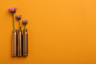 Photo of Beautiful flowers in bullet cases on orange background, flat lay. Space for text