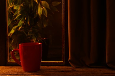 Photo of Red cup on wooden table near window indoors at night