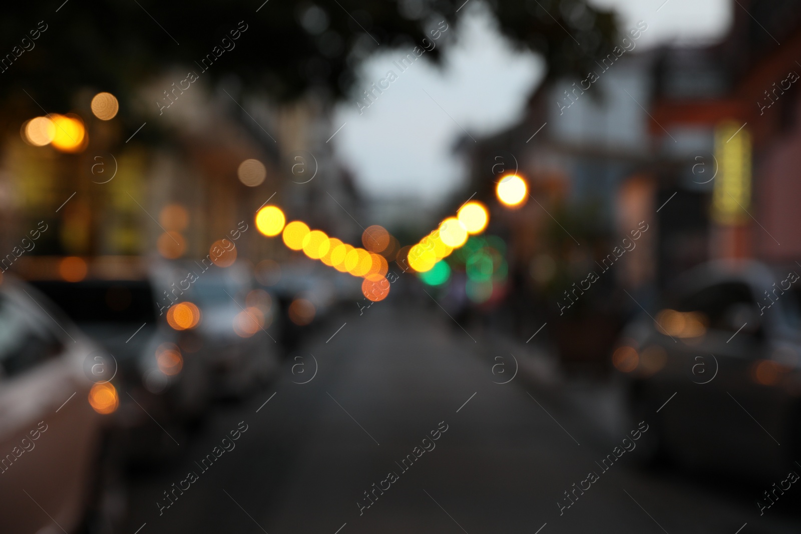 Photo of Blurred view of city street with parked cars in evening
