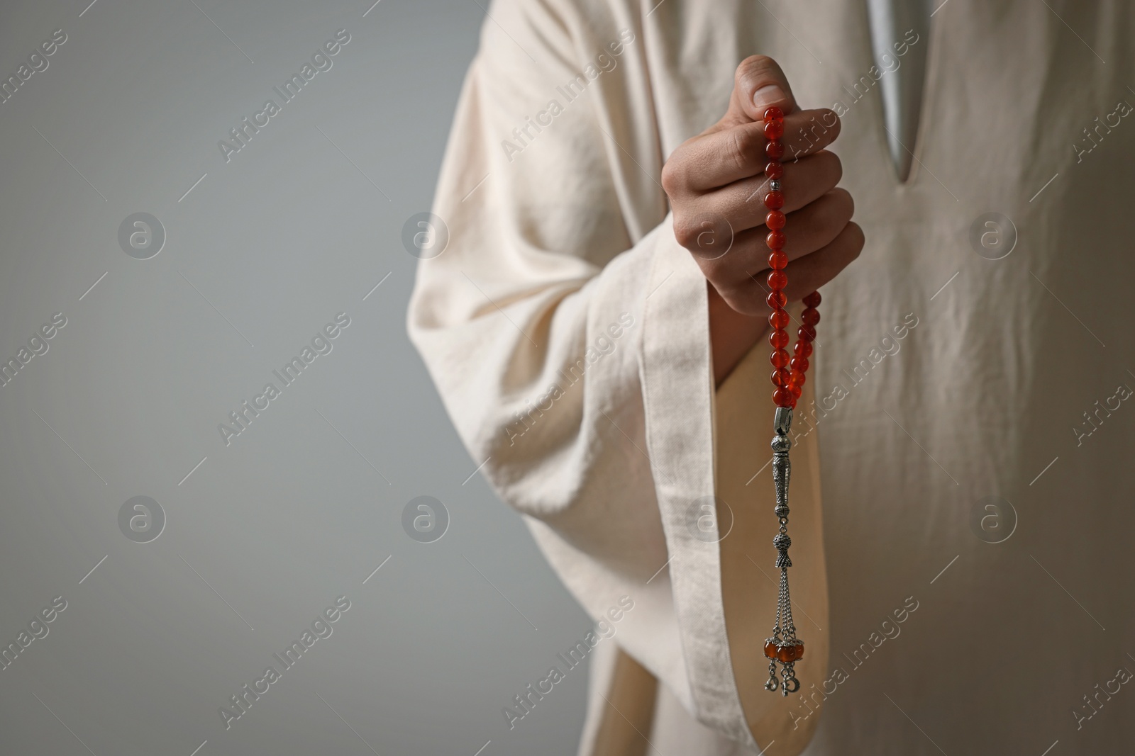 Photo of Muslim man holding misbaha on light grey background, closeup. Space for text