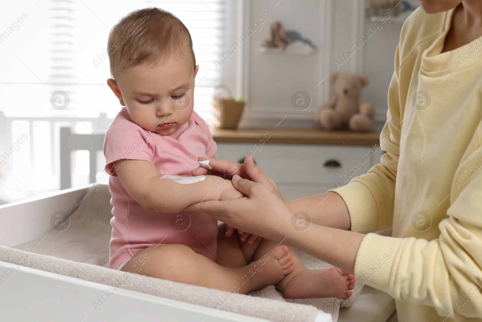 Photo of Mother applying body cream on her little baby at home, closeup