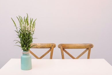 Vase with beautiful flowers on white table against color background. Stylish interior