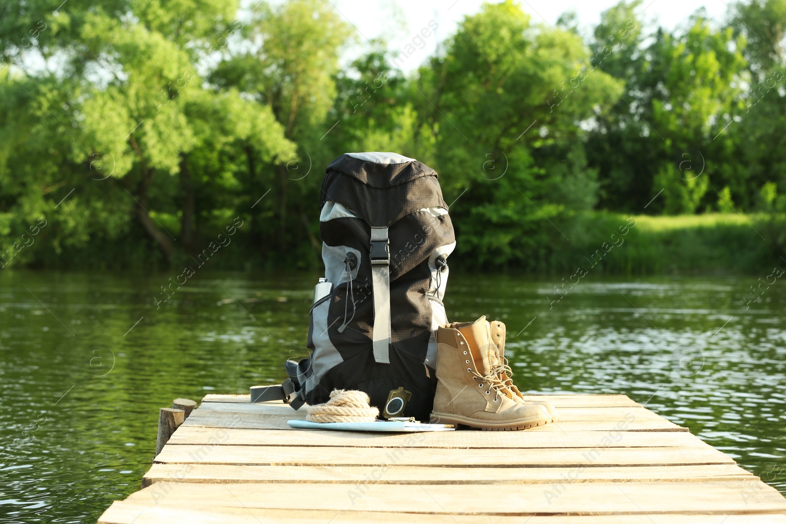 Photo of Backpack and camping equipment on wooden pier near river