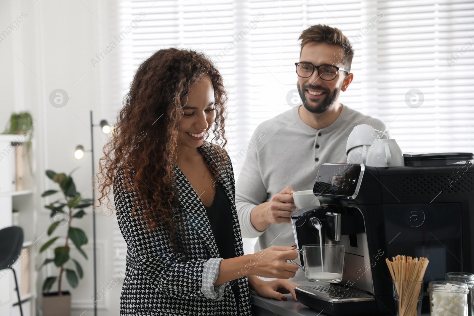 Photo of African-American woman talking with colleague while using modern coffee machine in office