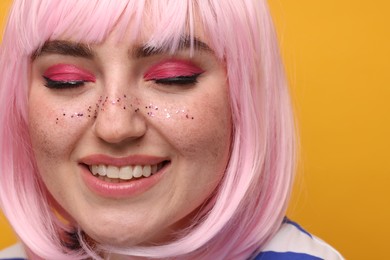 Smiling woman with bright makeup and glitter freckles on yellow background, closeup