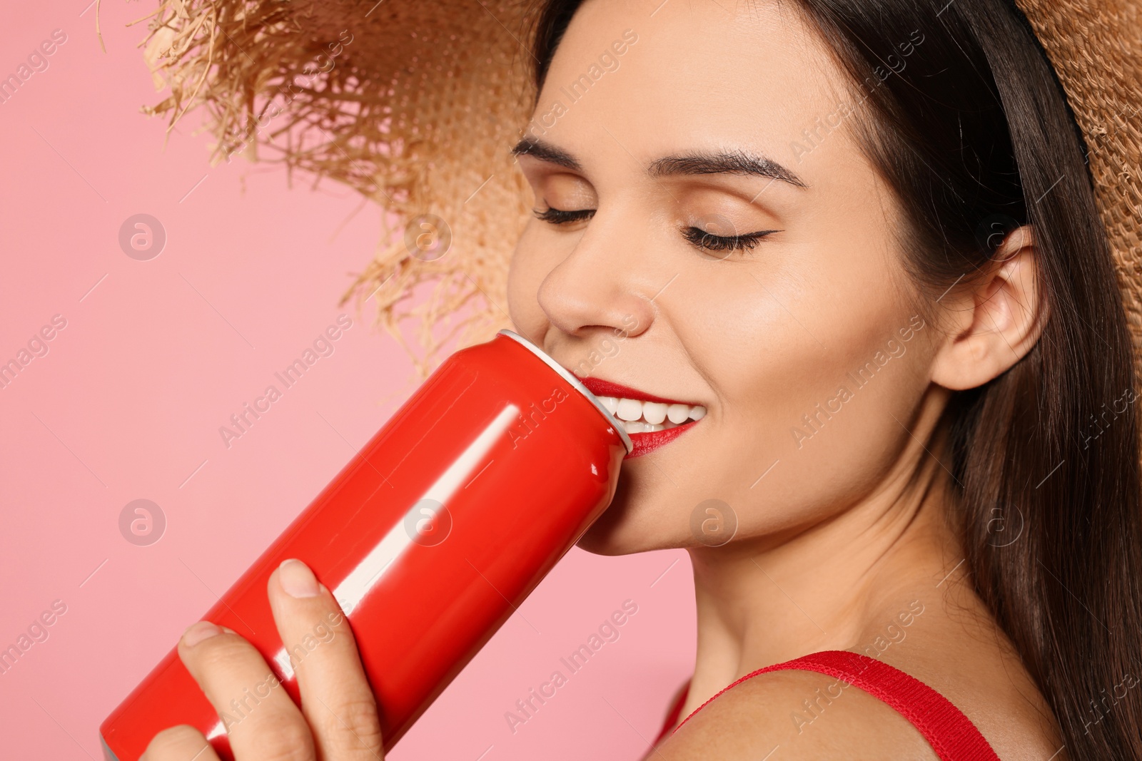 Photo of Beautiful young woman with straw hat drinking from tin can on pink background, closeup