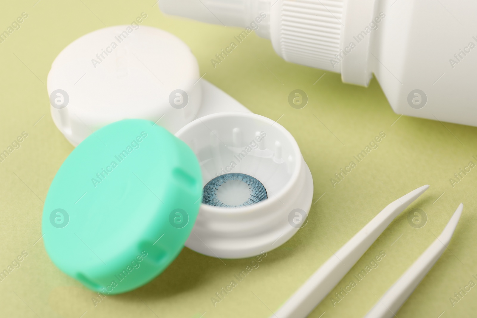 Photo of Case with blue contact lenses and tweezers on light green background