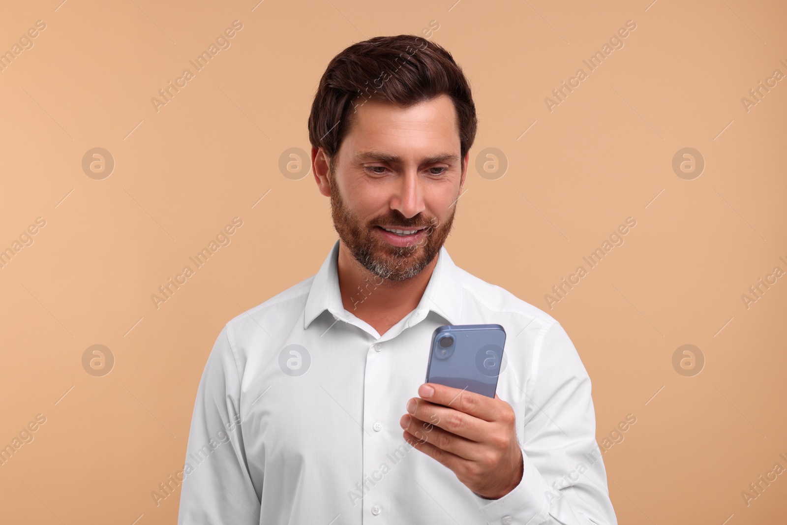 Photo of Handsome bearded man using smartphone on beige background