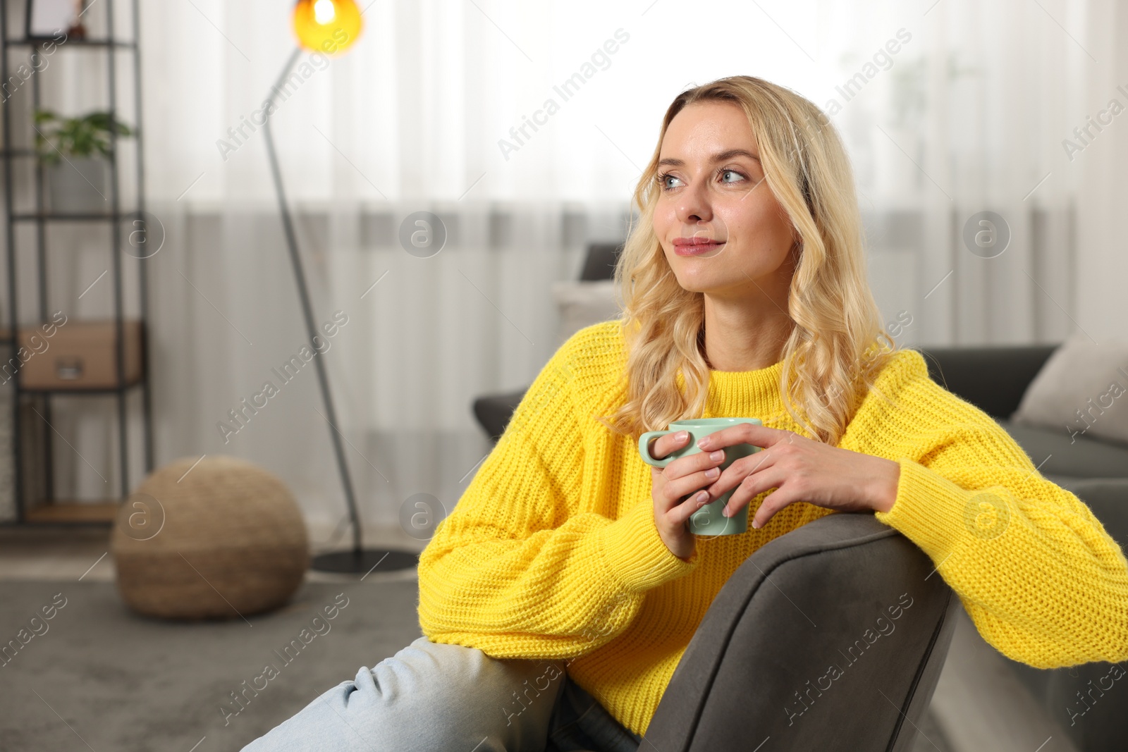 Photo of Beautiful woman in stylish warm sweater holding cup of drink at home. Space for text