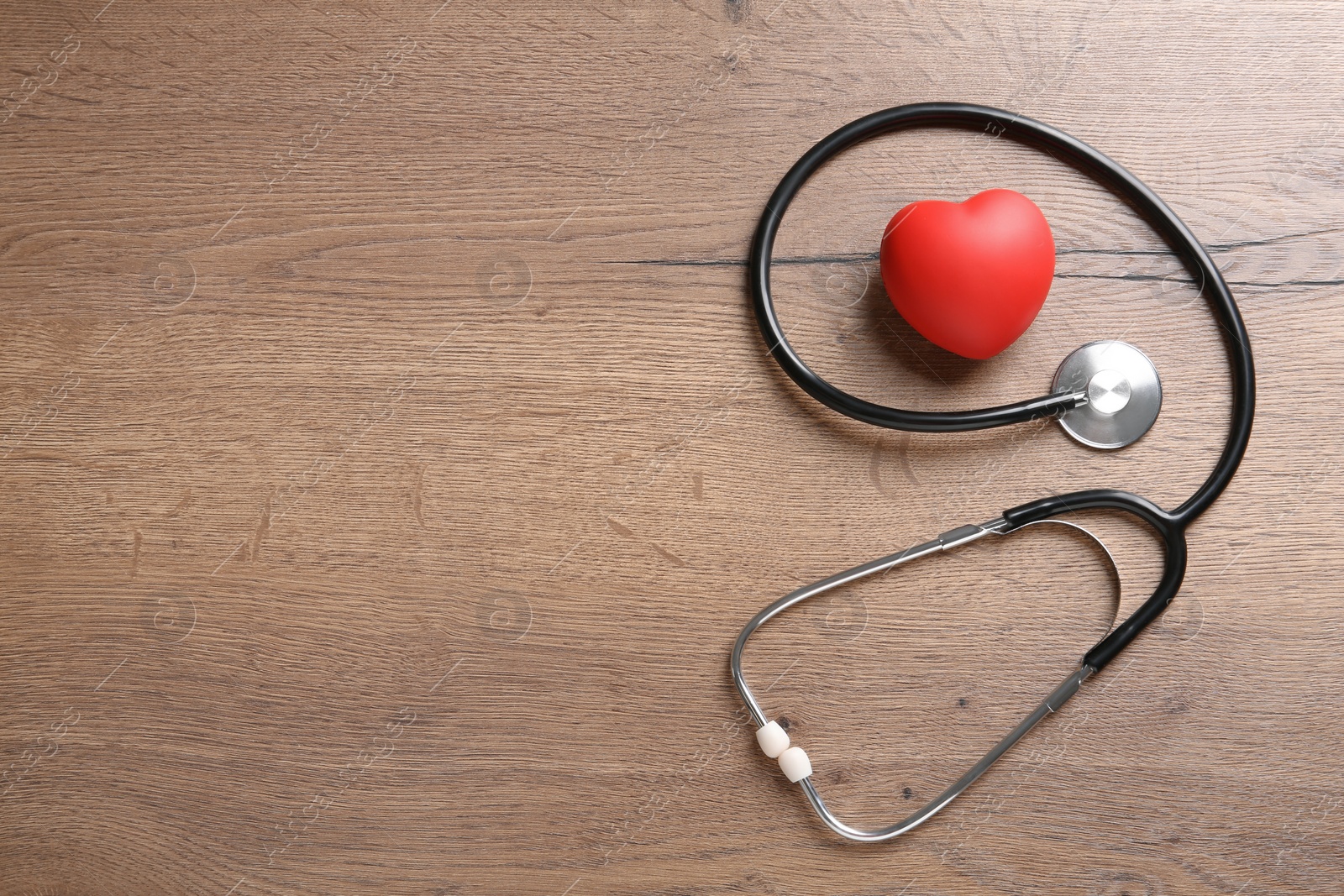 Photo of Stethoscope and red heart on wooden table, flat lay with space for text. Cardiology concept