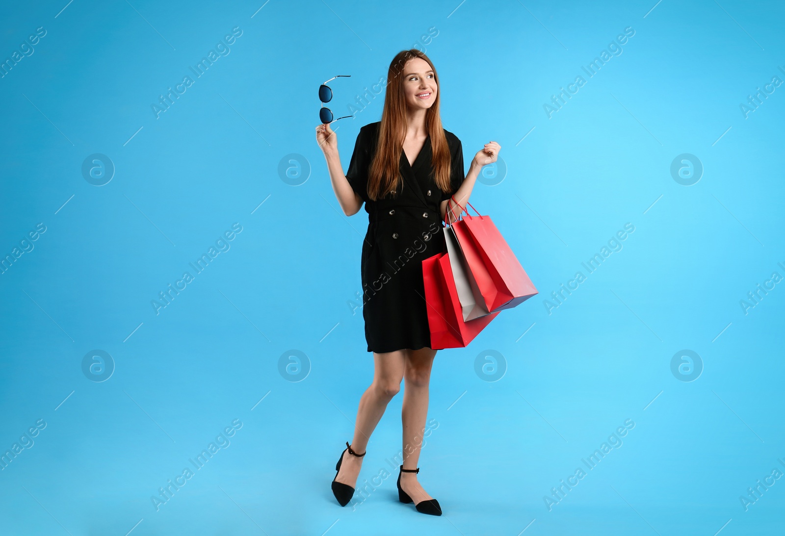 Photo of Beautiful young woman with paper shopping bags on light blue background