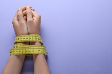 Woman tied with measuring tape on violet background, top view and space for text. Diet concept